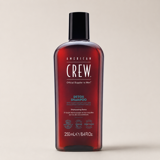 American Crew Detox Shampoo 250ml bottle at a three-quarter angle on a warm-grey studio background