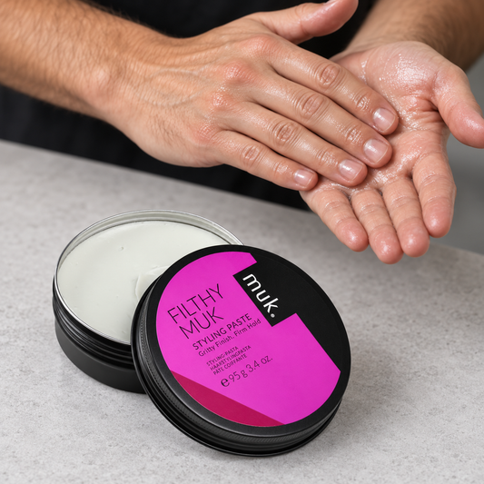 Hands emulsifying Filthy muk Styling Paste beside the open 95g tin before application.