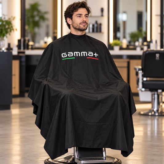 Gamma+ black cutting cape worn by a seated salon client, showing its drape and full hem.