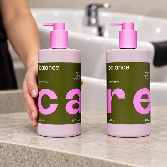 NAK Care Balance shampoo and conditioner 500 ml bottles beside a salon basin, with a stylist steadying the shampoo