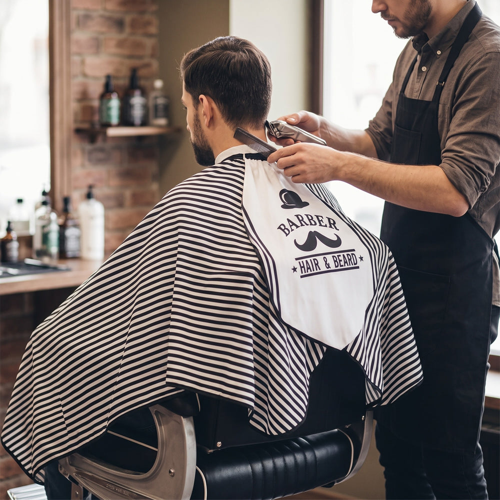 Barber cutting hair with client in RedOne Moe+Hat cape