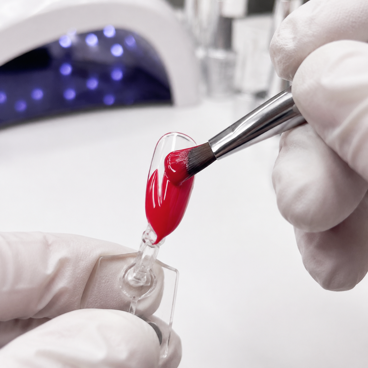 Nail technician applying ACOS HF019 Bright Red gel colour to a clear artificial practice tip