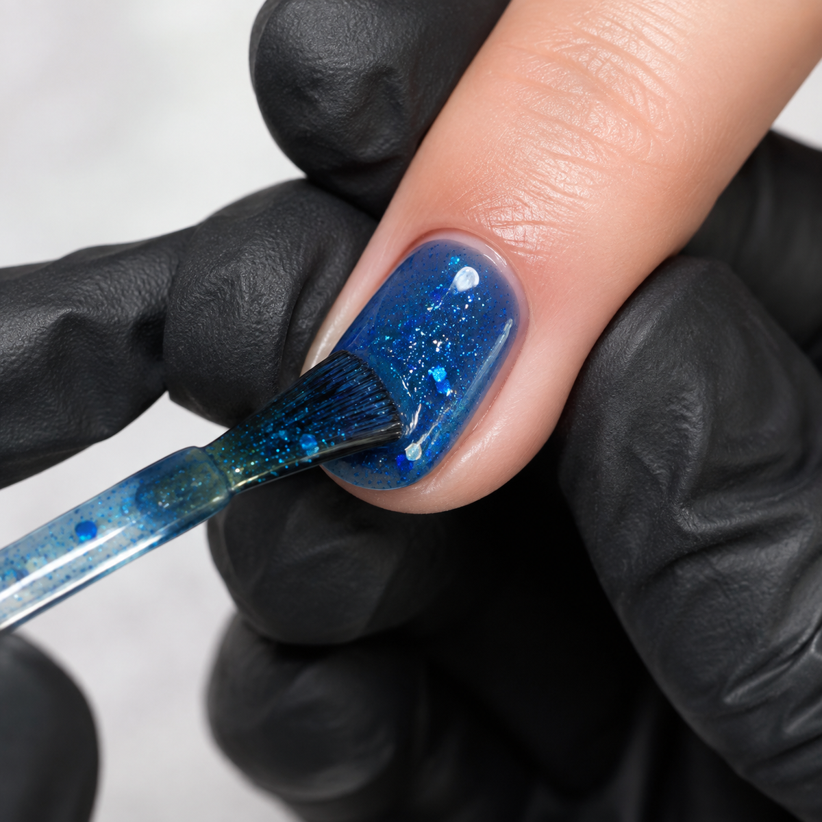 Professional applying ACOS Glossy Blue 101 transparent glitter gel to a prepared fingernail