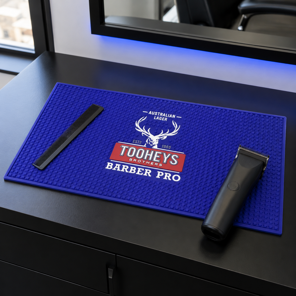 Blue Tooheys Barber Pro mat holding an unbranded clipper and comb on a barber workstation
