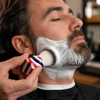 Barber applying shaving lather to an adult client's beard with the barber-pole brush