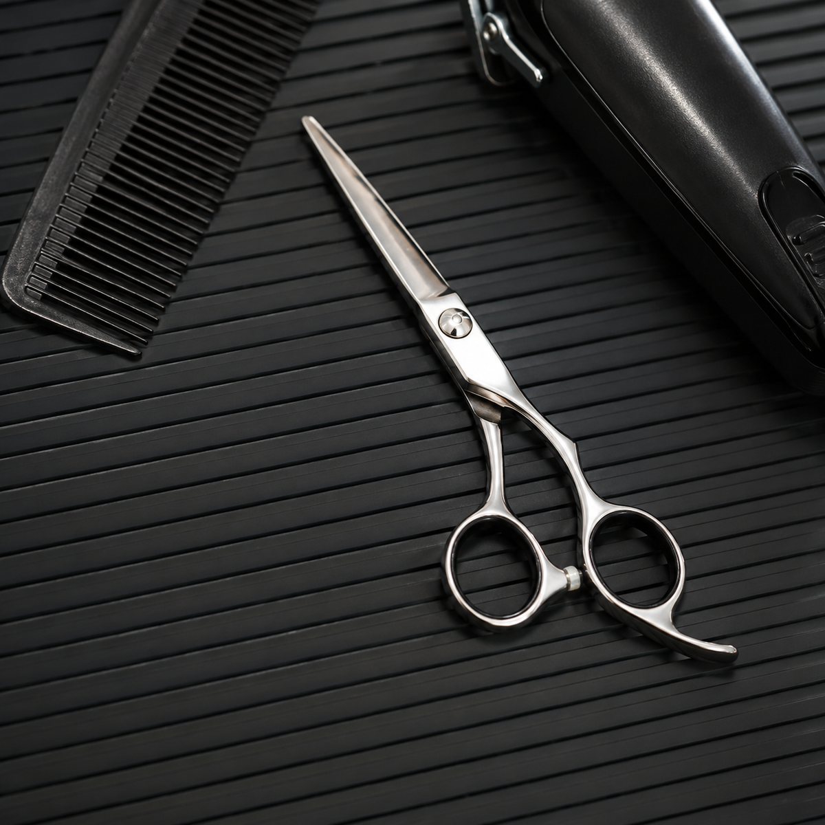 Close detail of comb, scissors and trimmer arranged on a black ribbed barber mat