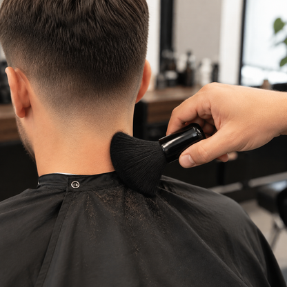 Barber using a black neck duster to sweep loose hair from a client’s neck