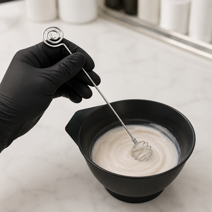 Gloved hand mixing cosmetic cream in a bowl with a stainless steel stick