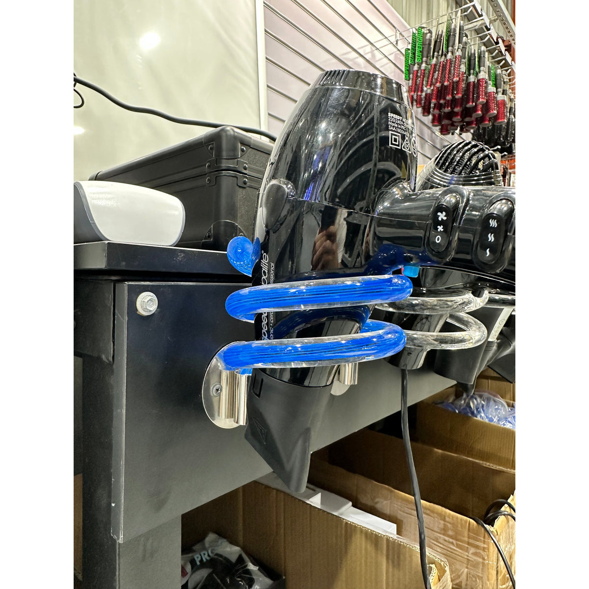 Blue wall-mounted hair dryer holder supporting a salon dryer at a styling station