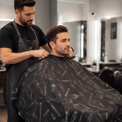 Barber securing a printed cape around an adult client’s shoulders