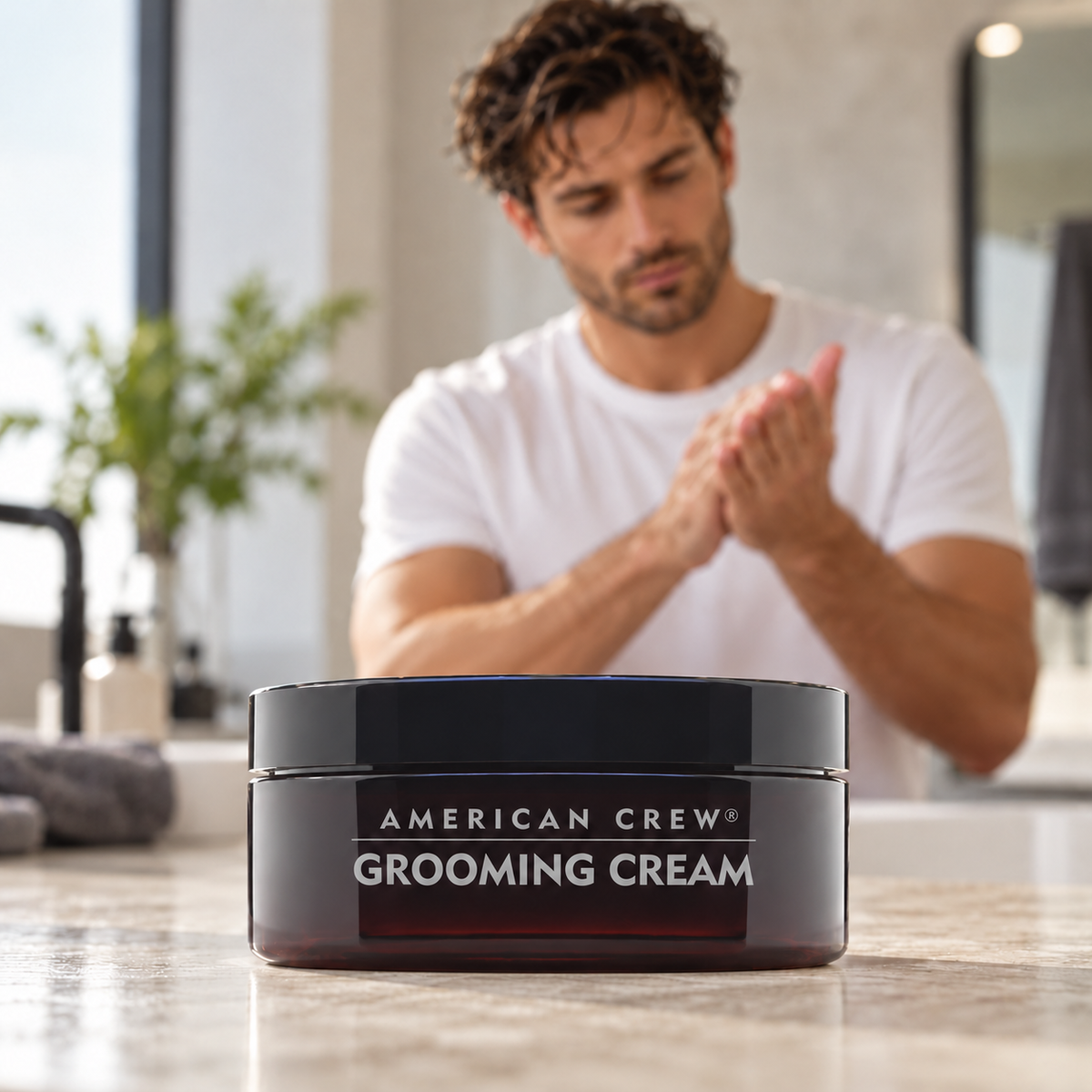 American Crew Grooming Cream 85g on a bathroom counter as a man spreads product between his palms.
