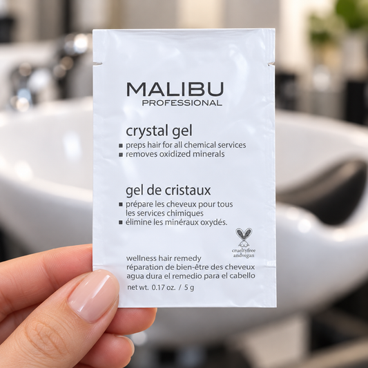 Malibu C Crystal Gel 5g sachet held by its edge at a salon basin