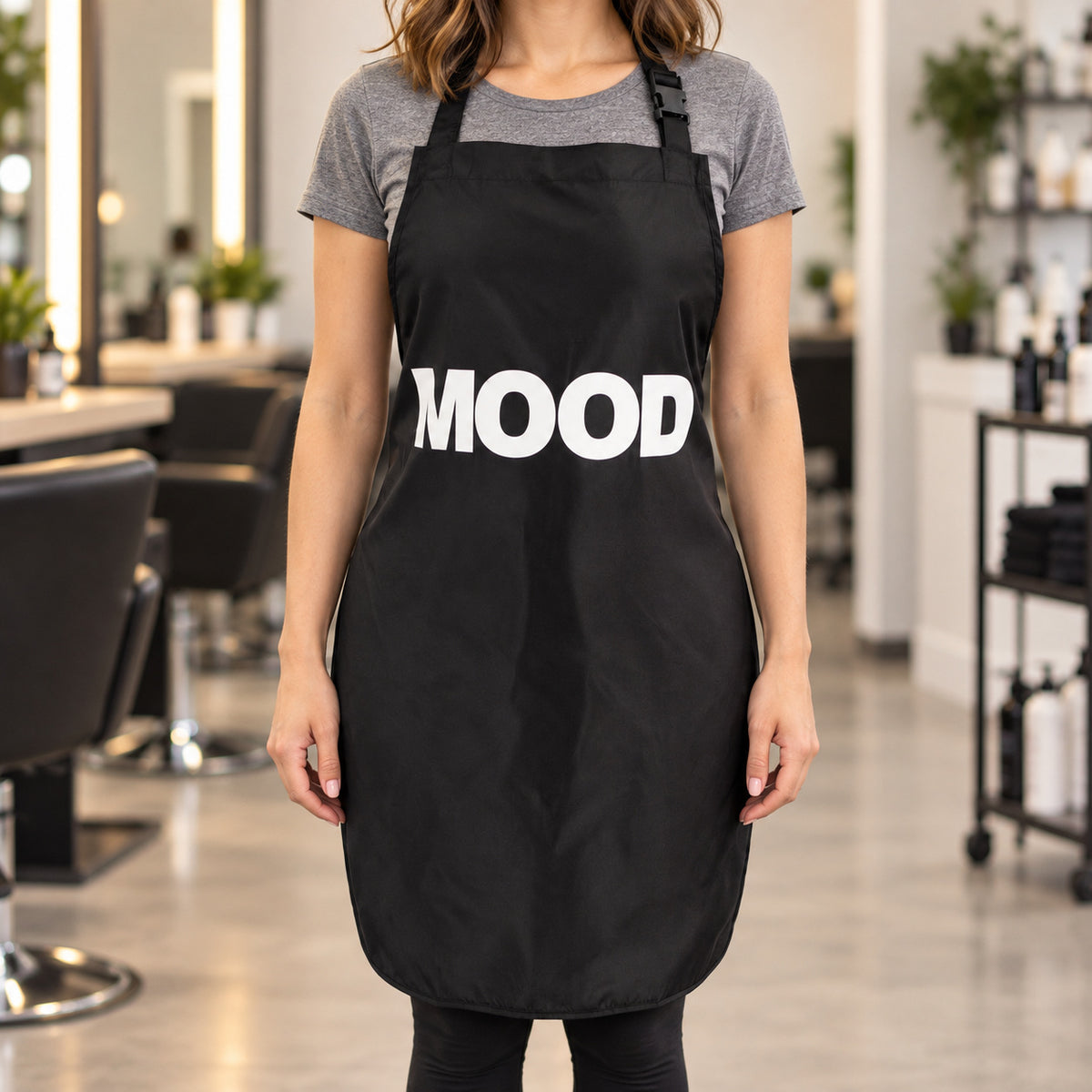 Stylist wearing the black MOOD apron, showing the front logo, neck buckle and rounded hem
