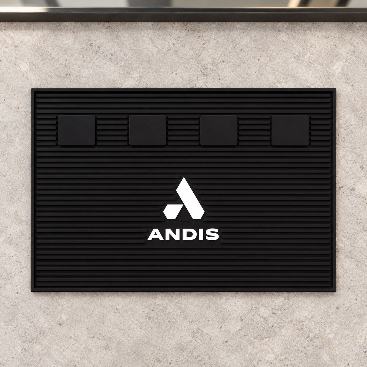 Andis black magnetic barber mat lying flat on a light stone workstation, showing four square pads and ribbed surface.