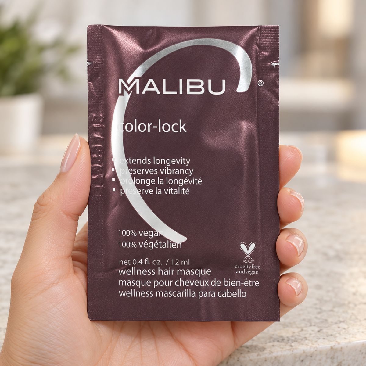 Malibu C Color-Lock Masque 12ml sachet held in a salon, showing the sealed front packaging.