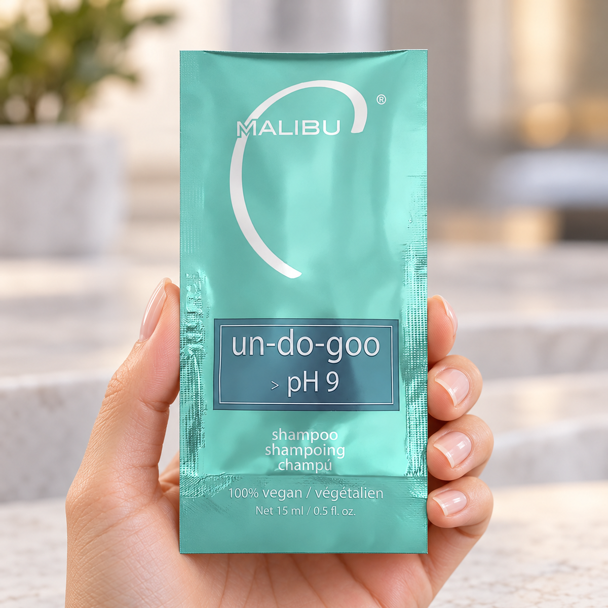 Malibu C Un-Do-Goo Shampoo 15ml sachet held in a salon, showing the sealed pack and label.