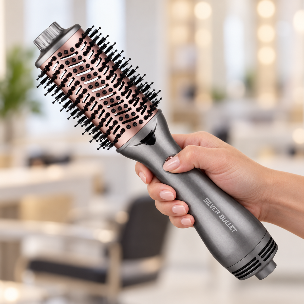 Hand holding the Silver Bullet Platinum 58mm Medium hot air brush, showing its handle and rose-gold barrel.