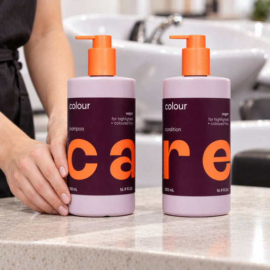 NAK Care Colour shampoo and conditioner 500 ml bottles beside a salon basin, with a stylist steadying the shampoo