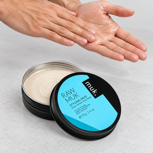 Hands emulsifying Raw muk Styling Mud beside the open 95g tin before application.