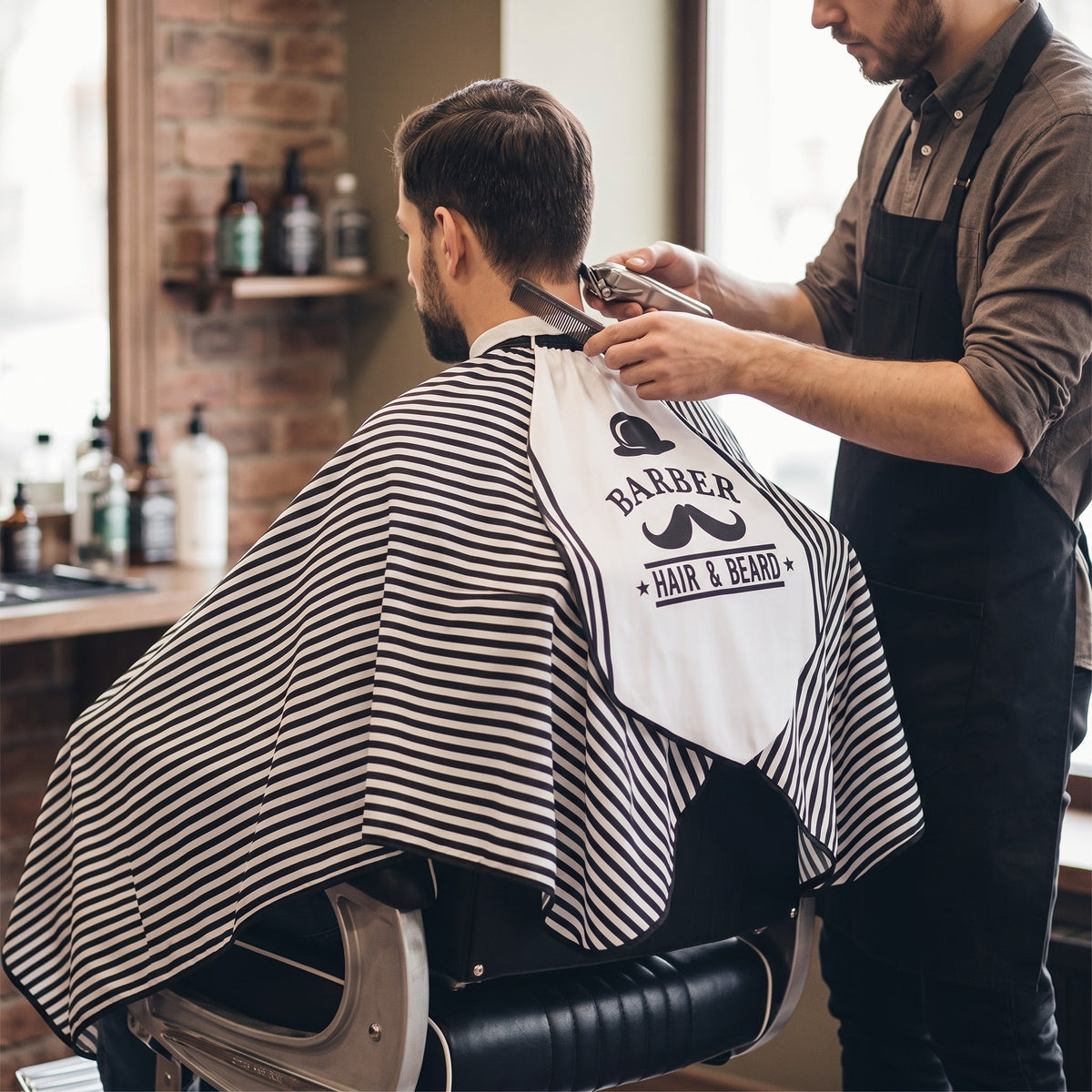 Barber cutting hair with client in RedOne Moe+Hat cape