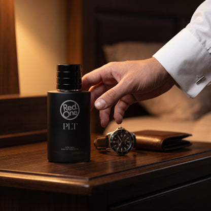 RedOne PLT men's perfume 100ml bottle on a dark wooden dresser beside a watch